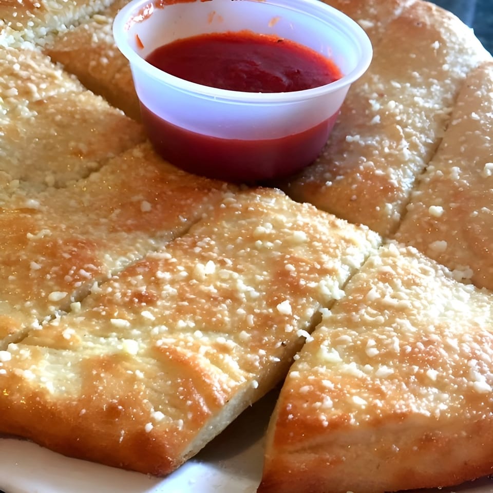 Close-up of Mancino's of Taylor's cheesy breadsticks with a side of red dipping sauce.