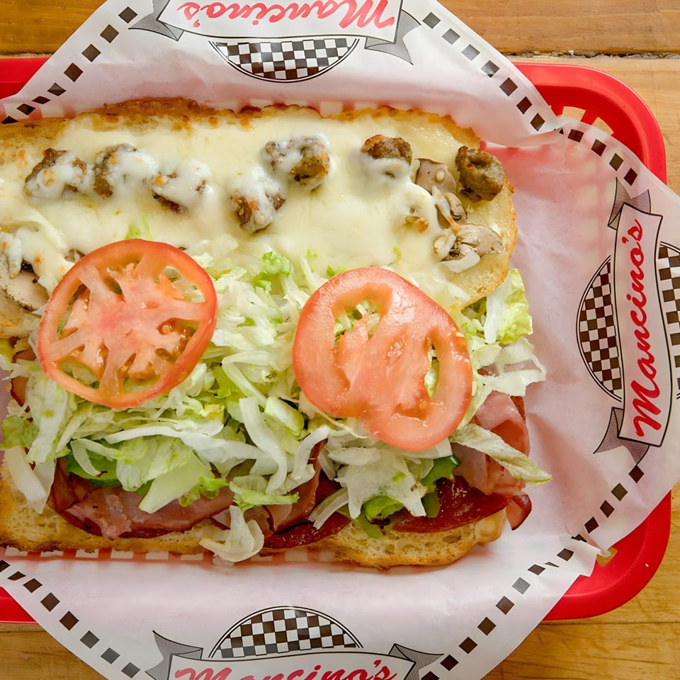 A Mancino's grinder sandwich with melted cheese, sausage, mushrooms, lettuce, tomatoes, and deli meats.
